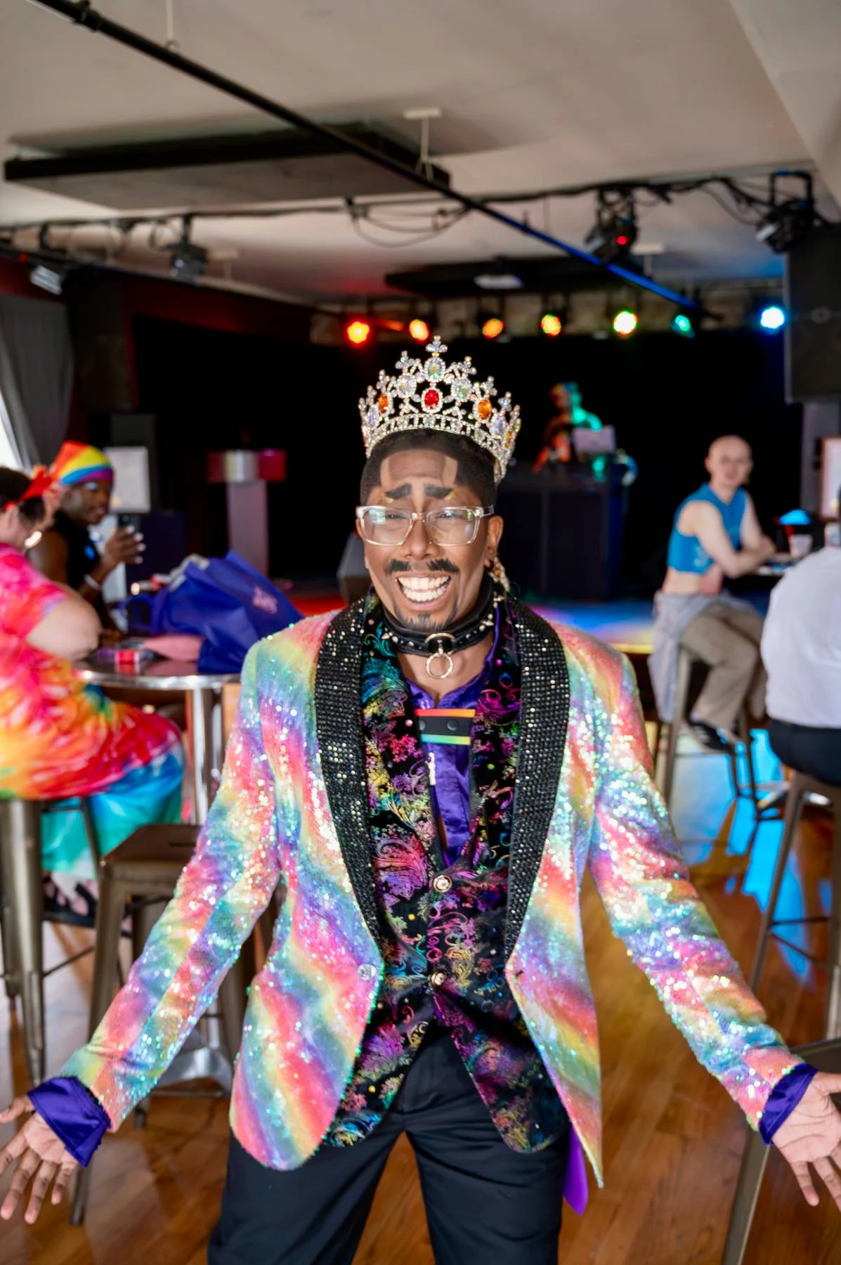 A crowned performer in a rainbow sequin jacket